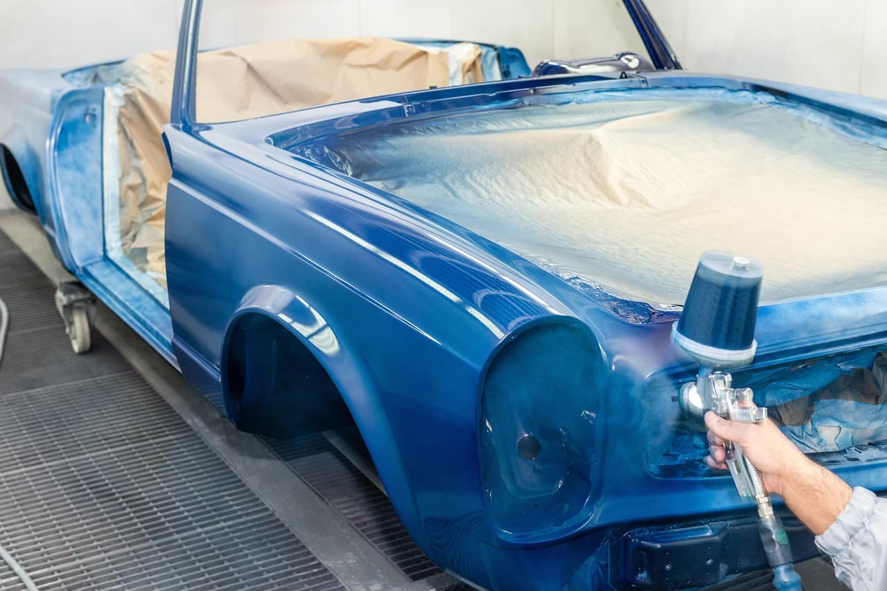 A painter spraying a blue car body in a spray booth