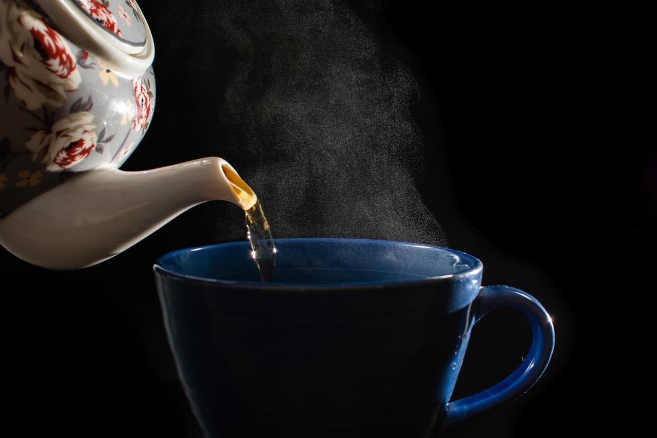 Tea being poured from a pot into a navy blue cup
